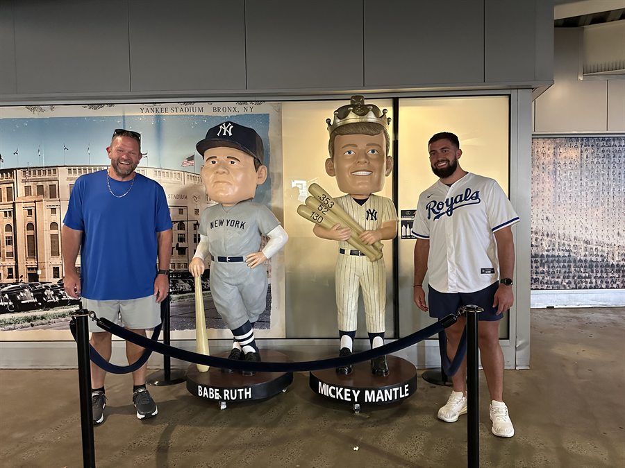 Chase Dalton, right, in a Kansas City Royals jersey at a ballpark, beside
                      oversized Babe Ruth and Mickey Mantle figures